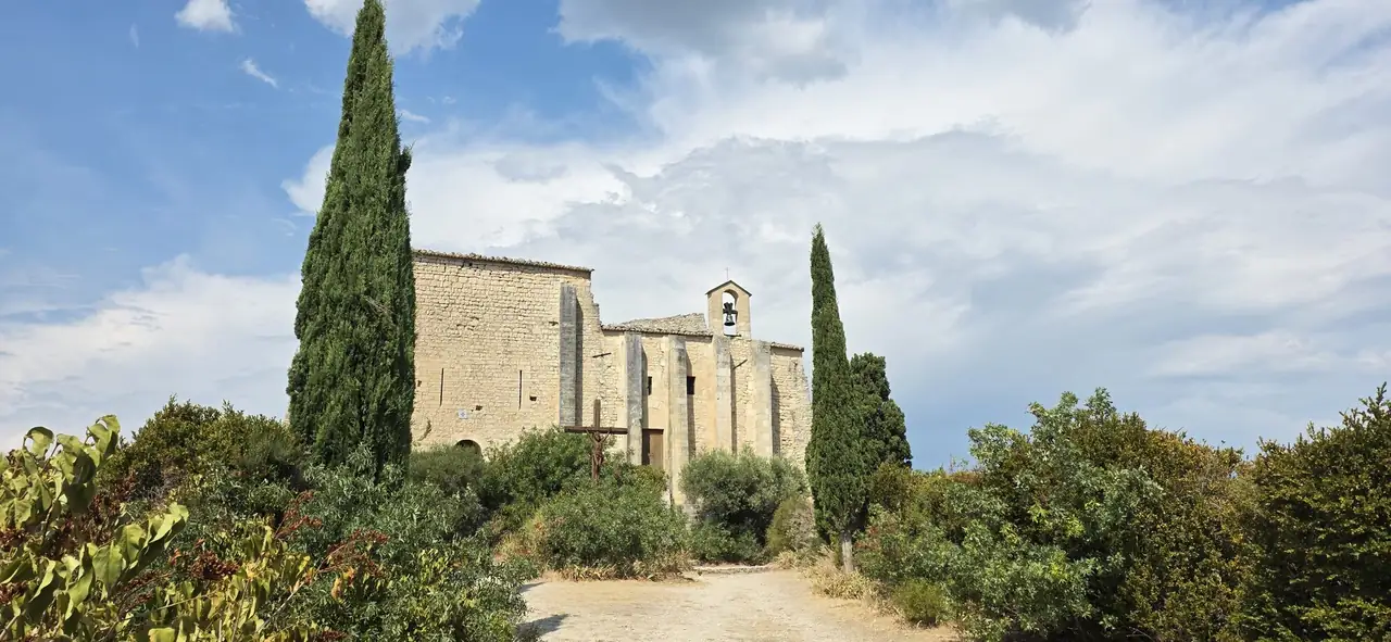 A stone chapel framed by cypress trees under a summer sky