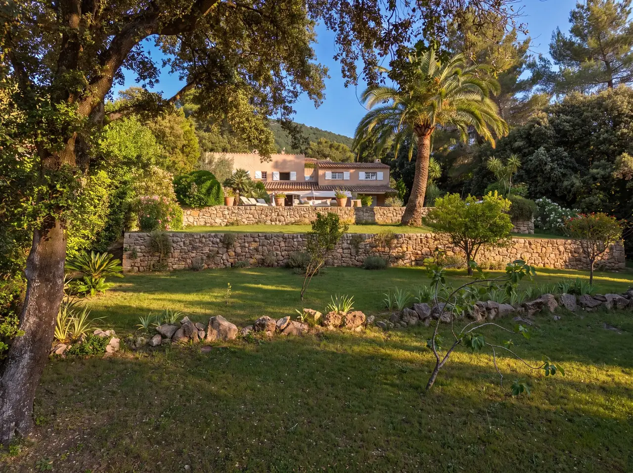 Terraced garden edged with dry-stone walls, a palm tree and a Provençal bastide in the late afternoon